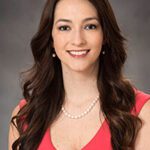 A headshot of Chelsie Dubay wearing a light red top in front of a gray background