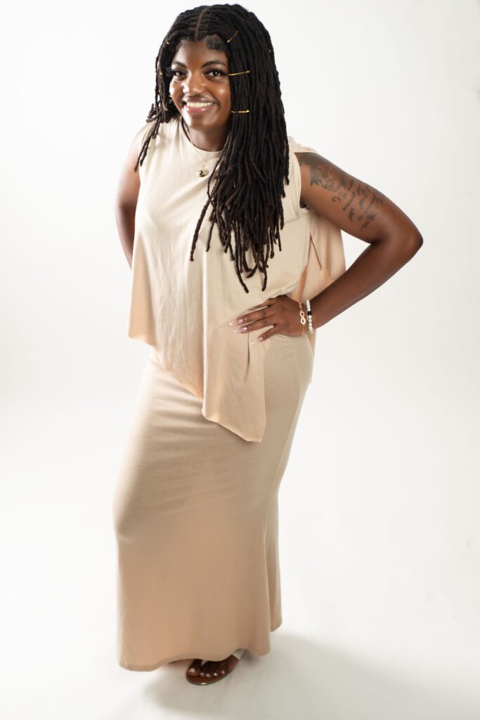 NCWIT AiC Stories Ambassador Neith Reid-EL in a long, cream dress smiling toward the camera