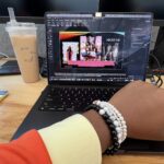 Vivid photo of Neith’s arm — in an orange blazer and four beaded bracelets — across her black work laptop with an iced coffee to the left, while at her desk as an Amazon intern in Seattle, Washington