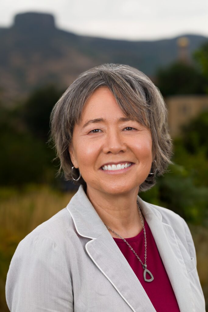 A photo of Stefanie Tompkins smiling at the camera in front of a mountain landscape